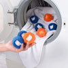 A hand is placing reusable pet hair and lint removal balls in the drum of a white washing machine.