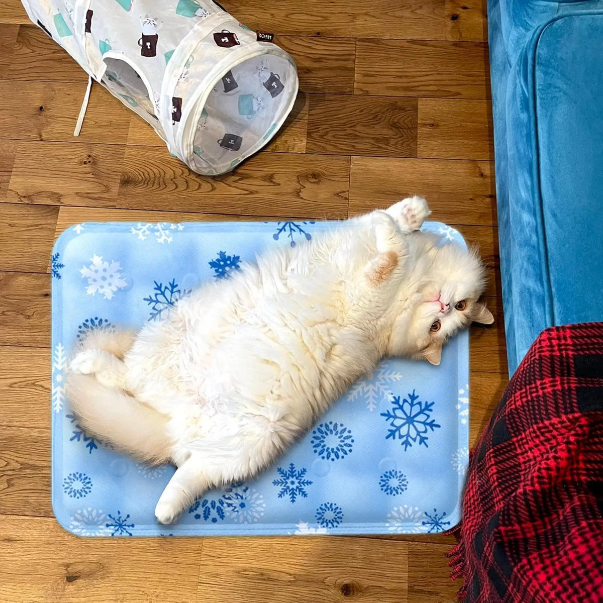 A fluffy white cat is relaxing on a blue pet cooling mat on a wooden floor.