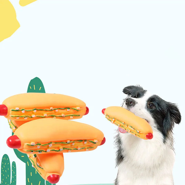 A dog is holding a large, orange hot dog squeaky chew toy.