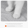 A close-up view of a white cat paw resting on a gray litter mat surface.