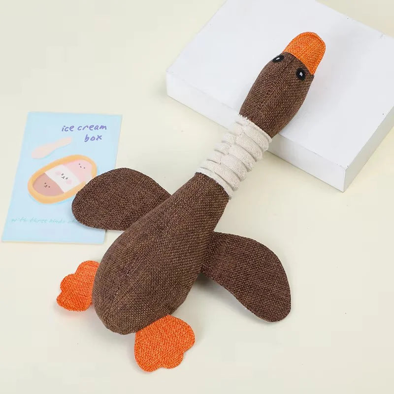 A brown plush toy shaped like a duck with orange feet and an orange beak, resting on a white box.