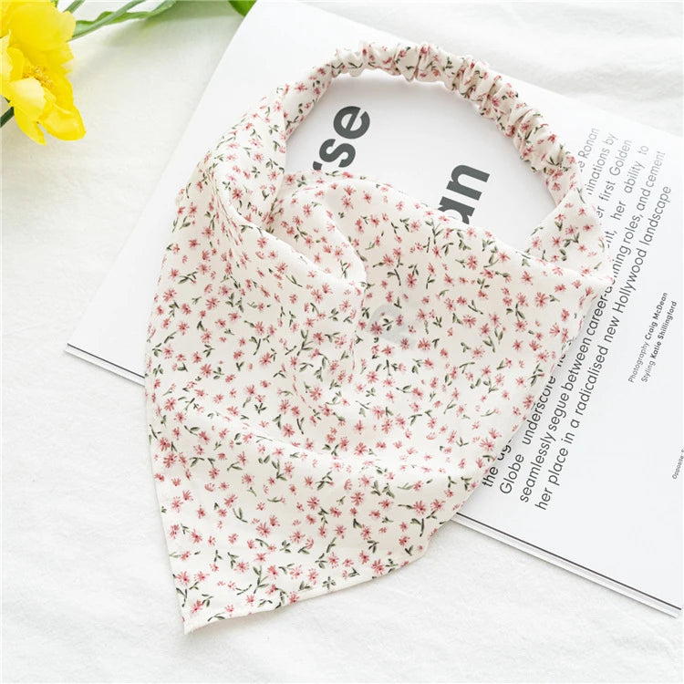 A pink floral patterned triangle head scarf is displayed on a white surface next to a magazine.