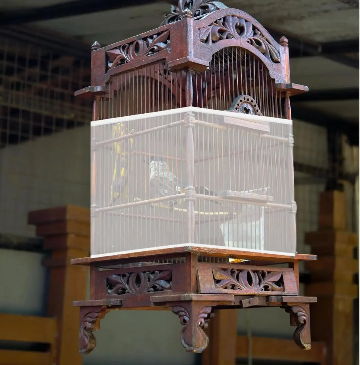 A vintage wooden bird cage with a clear plastic seed guard net and decorative metalwork.