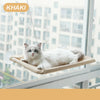 A white cat is relaxing on an aerial hammock pet bed suspended in a bright indoor setting.