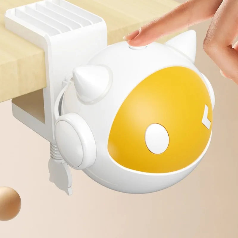 A white automatic lifting cat toy ball with yellow accents is being held by a hand above a wooden surface.
