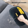 A hand wearing a black silicone glove with yellow accents is removing pet hair from a gray fabric surface.