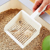 A hand is using an extra-large white cat litter scoop with a hanging hook to scoop litter from a box of wood pellets.