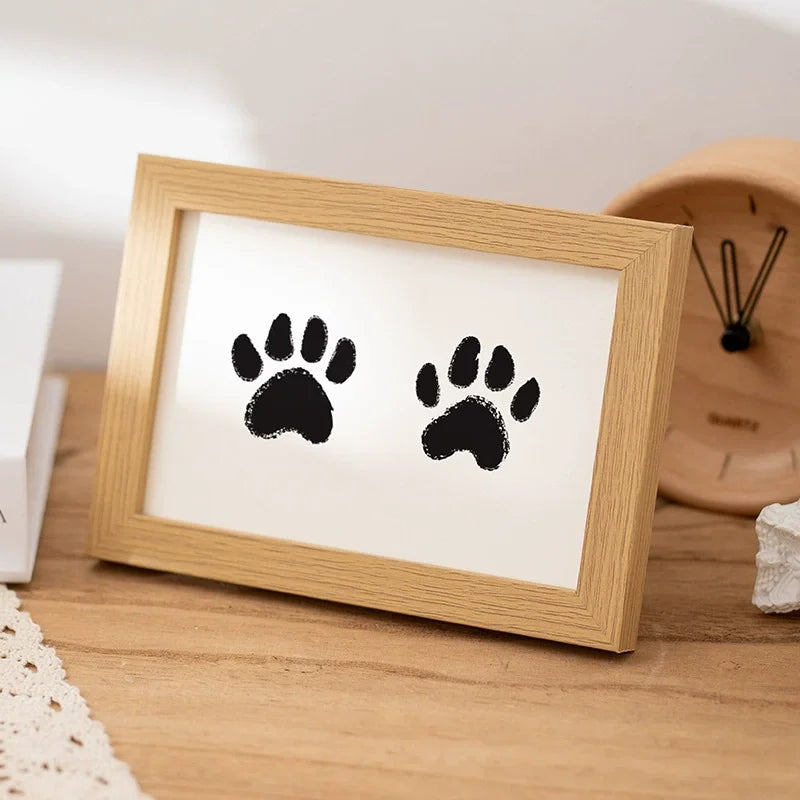 A wooden photo frame displaying two black paw prints on a white background.