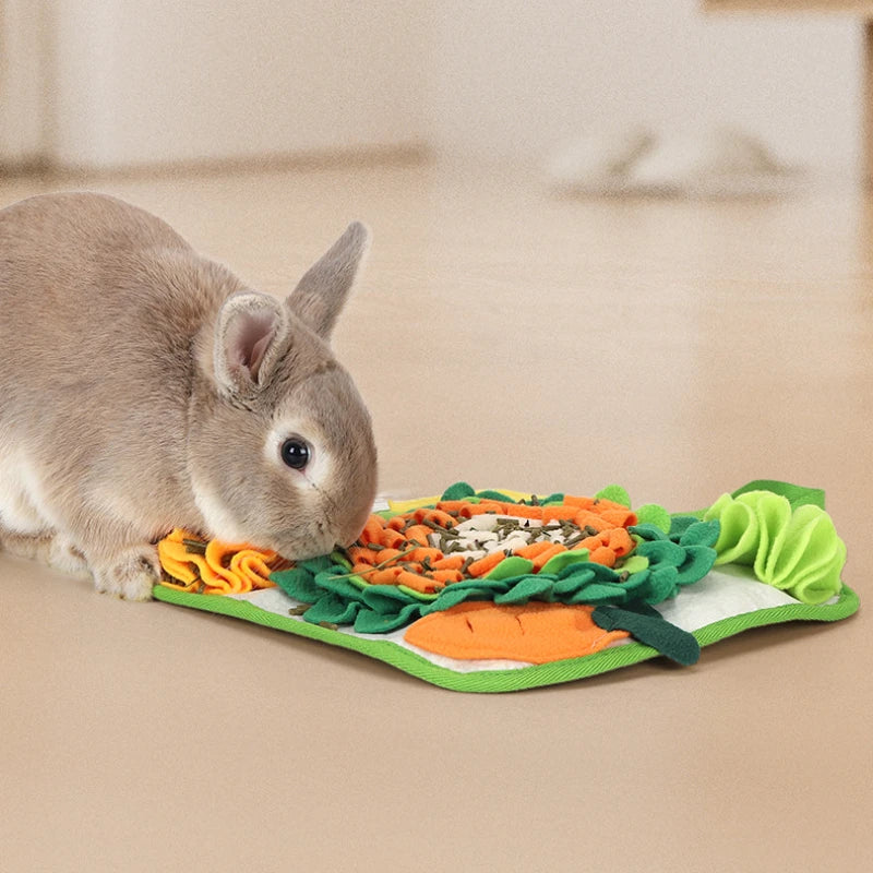 A small gray rabbit is sniffing a mat filled with various vegetables like carrots and greens.
