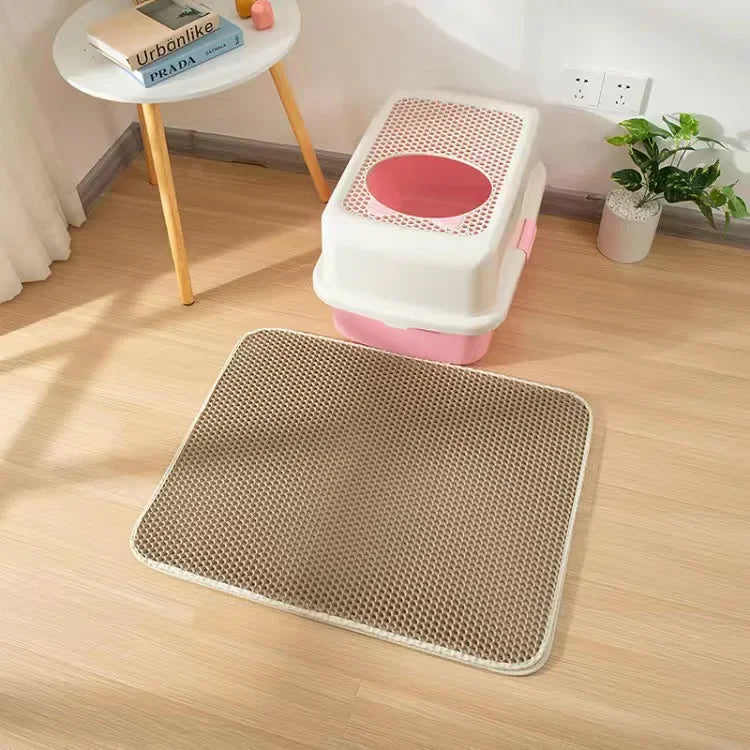 A pink and white double-layer cat litter mat with a waterproof base is placed on a light wood floor.