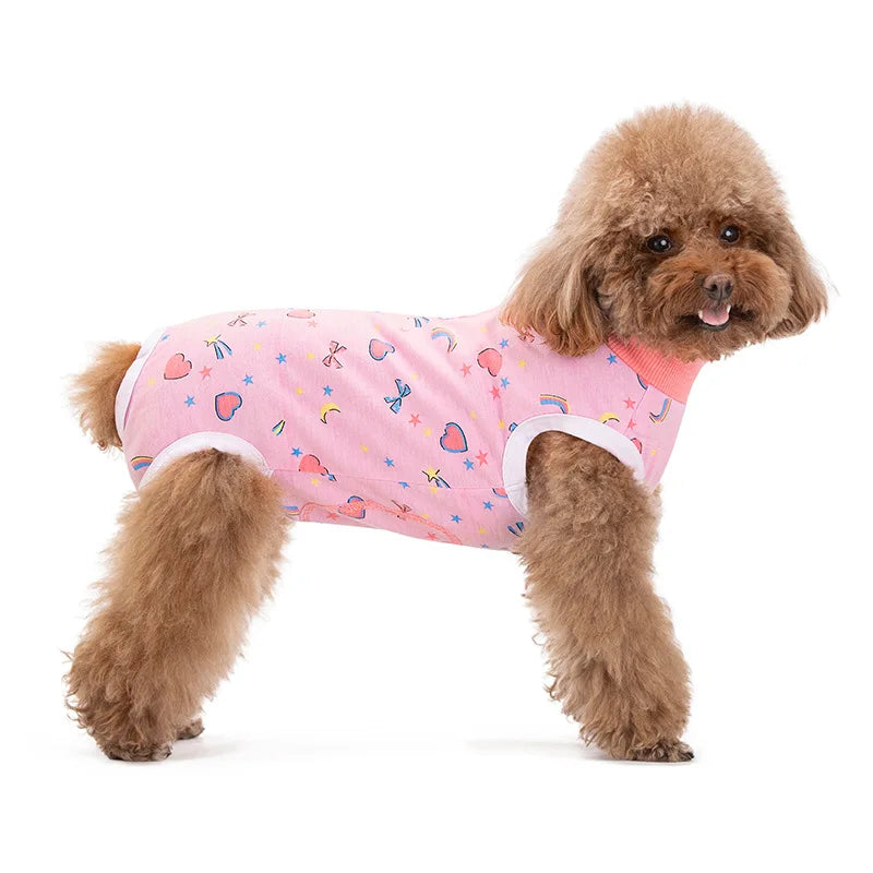 A fluffy brown dog wearing a pink cotton recovery suit decorated with various fabric patterns.