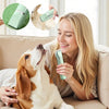 A woman is holding a green pet grooming kit while a dog looks up at her.