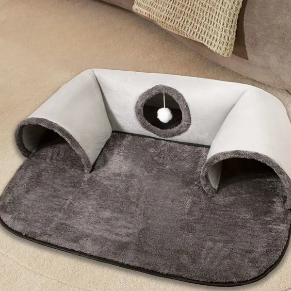 A gray U-shaped tunnel cat bed with a round entrance and soft lining on a light colored surface.
