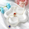 Un délicat collier de perles avec un pendentif de pierre rouge est présenté sur un plat en céramique blanche.