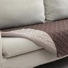 A pink quilted pet mat with a white non-slip base resting on a light-colored sofa cushion.