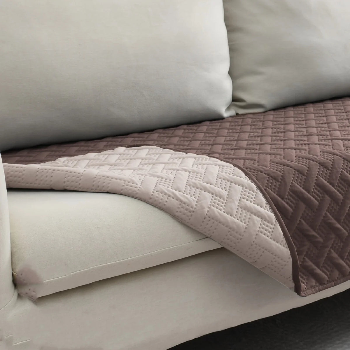 A pink quilted pet mat with a white non-slip base resting on a light-colored sofa cushion.