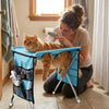 A woman is using a foldable pet grooming hammock to bathe and trim a orange cat.