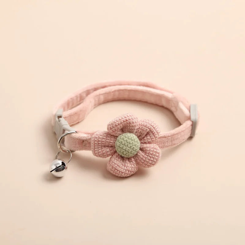 A pink knitted floral cat collar with a green flower accent and silver bell.