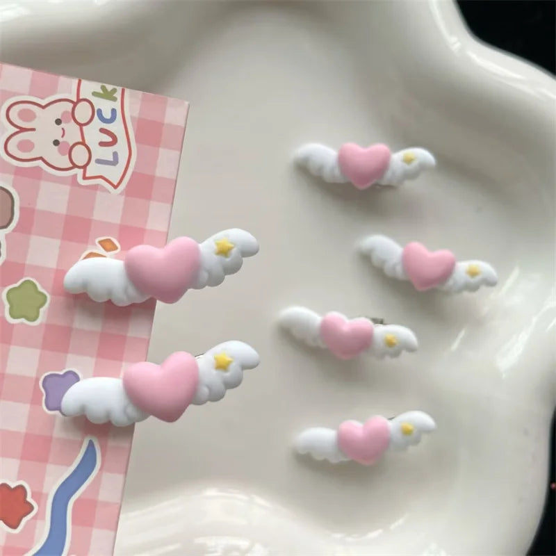 Pink and white pet hair clips shaped like angels are displayed on a white plate next to pink patterned paper.