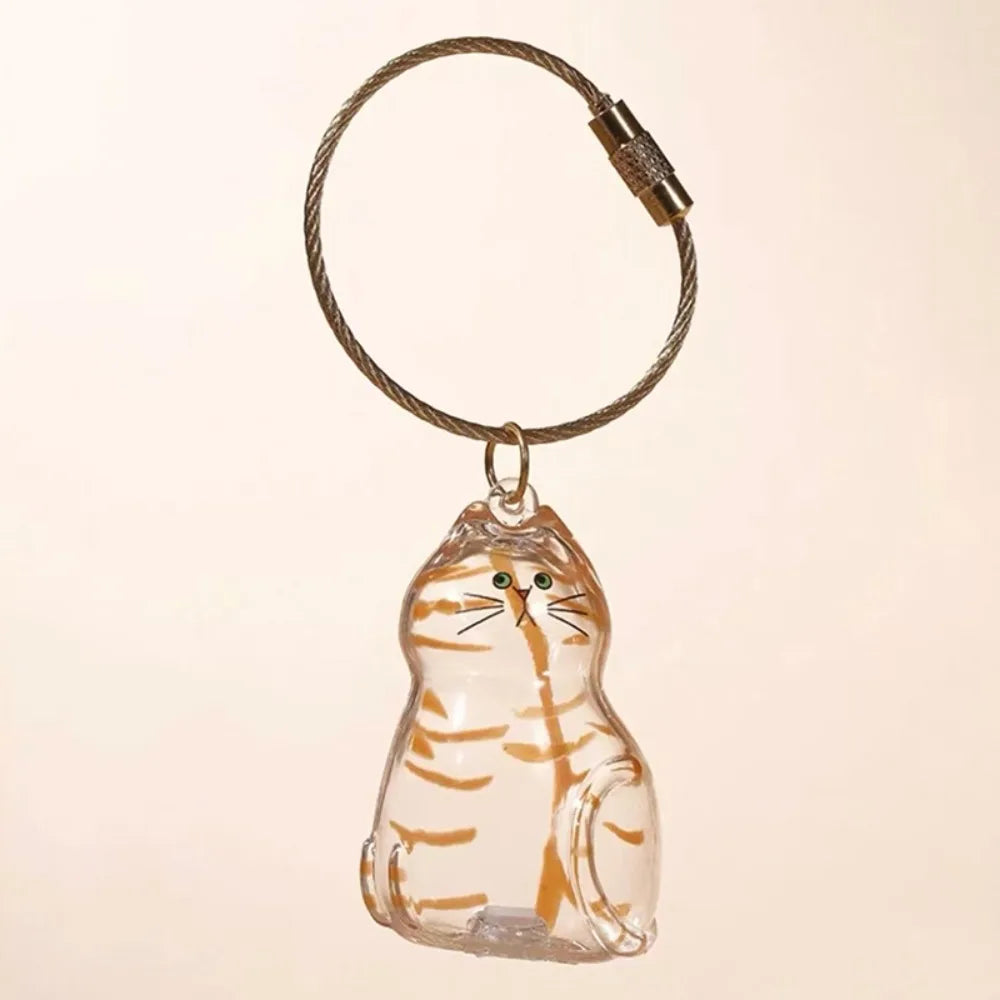 A clear glass figurine of a striped cat is attached to a braided leather keychain.