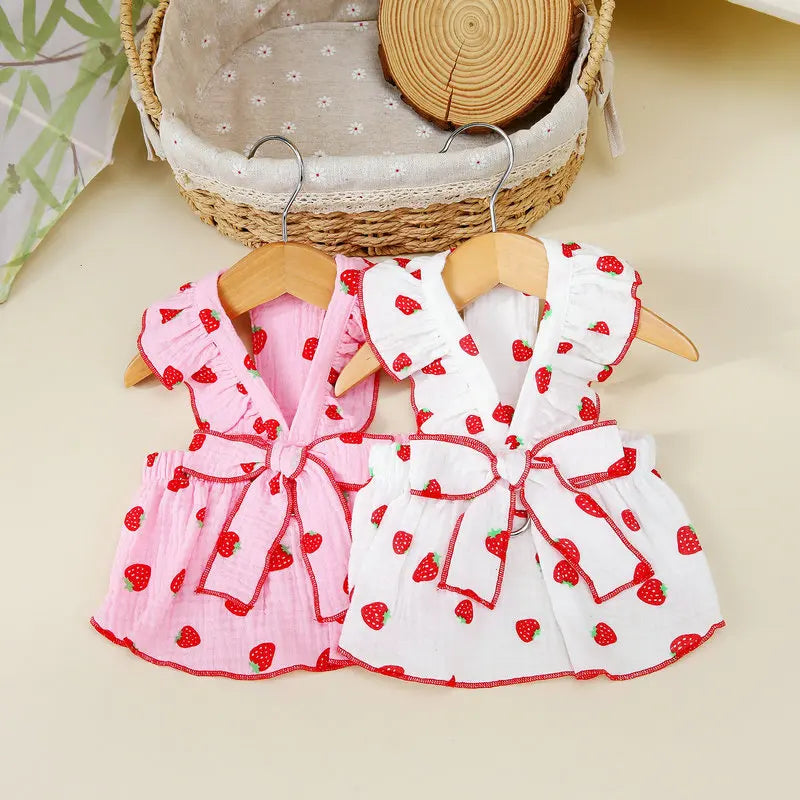 A pink and white strawberry print dress for a dog displayed on a wooden hanger.