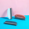 A collection of three portable lint and pet hair remover brushes in white, terracotta, and dark gray against a pink and blue 