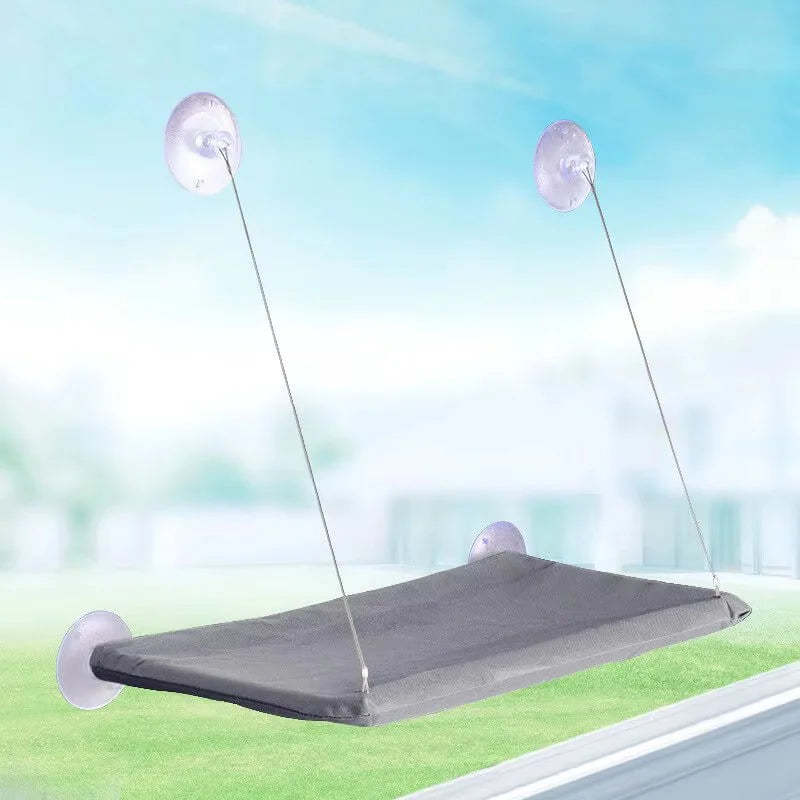A gray hammock bed suspended by thin lines above a green surface, featuring clear suction cup windows.
