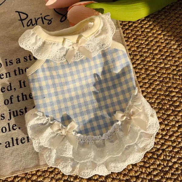 A white and blue gingham pet dress with lace trim and a bow collar displayed on a light fabric background.