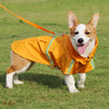 A light brown and white dog wearing a yellow waterproof raincoat with reflective stripes, standing on green grass.