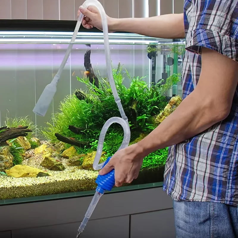 A person uses an aquarium siphon gravel cleaner with a water change pump to clean the substrate of a fish tank.