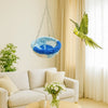 A yellow bird is perched on a hanging hammock made of blue and white fabric in a bright room.