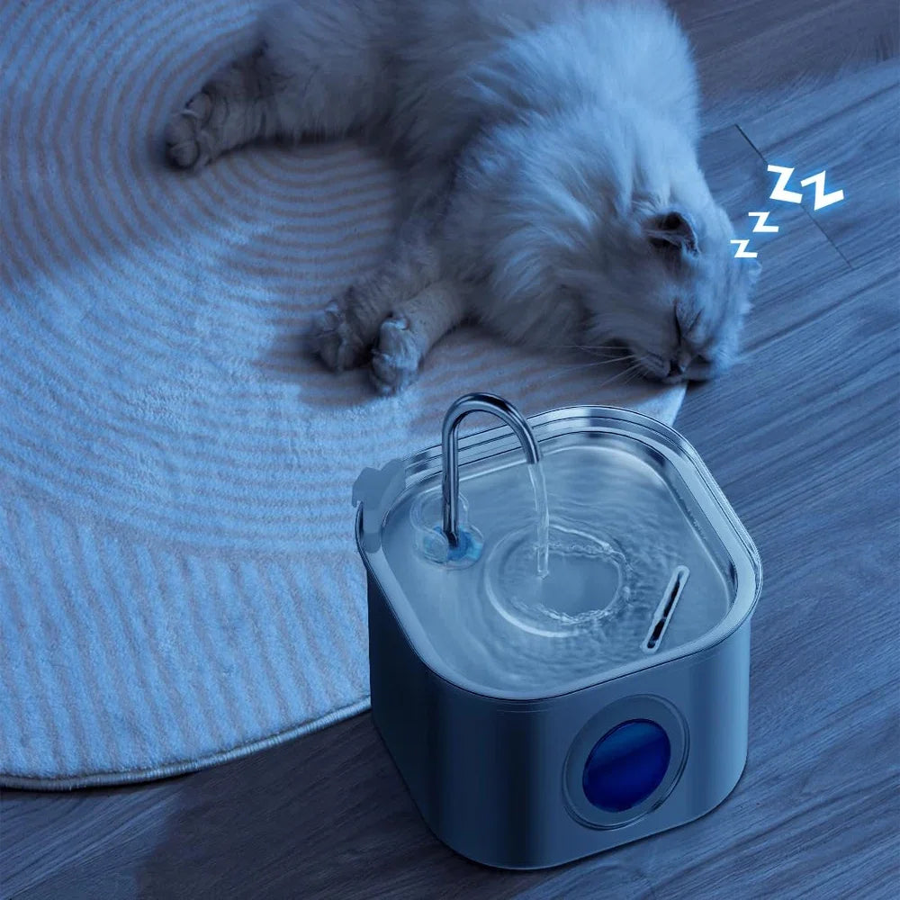 A fluffy gray cat is resting near a stainless steel pet water fountain with a blue visual window.