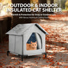A gray insulated cat shelter with an entrance, featuring a cat inside, placed outdoors on a leaf-covered path.