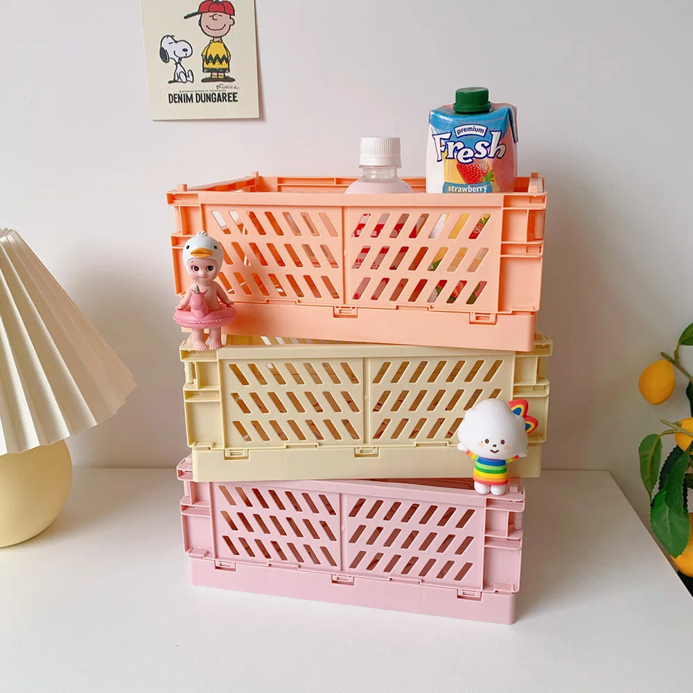 Eine Stapel rosa und orangefarbener Plastik-Aufbewahrungskörbe mit kleinen Puppen und einer Farbtube auf einer weißen Oberflä