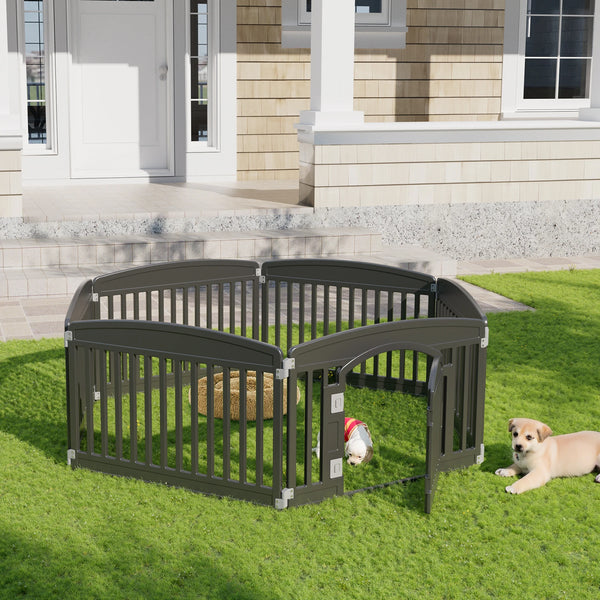 A dark gray expandable plastic dog playpen is set up on a green lawn with a small dog nearby.