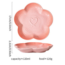 A pink ceramic pet bowl with ridges and a heart design shown next to its wooden stand.