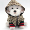 A white dog wearing a beige patterned hooded jacket with black trim.