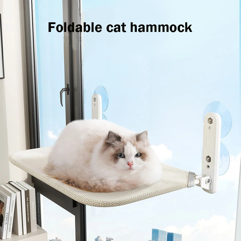 A fluffy white and gray cat is relaxing on a foldable cat hammock mounted on a window sill.