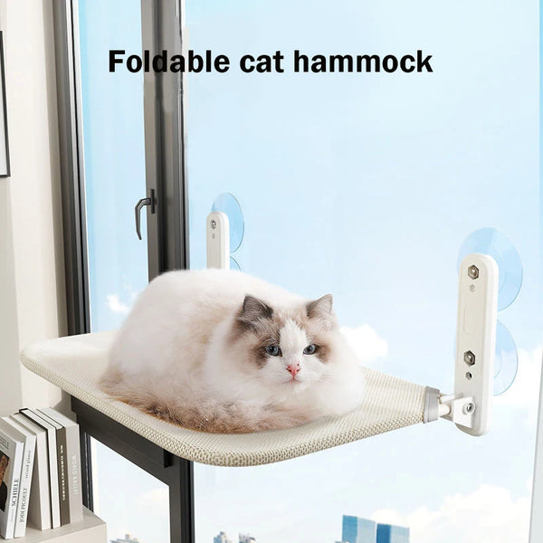 A fluffy white and gray cat is relaxing on a foldable cat hammock mounted on a window sill.