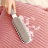 Una mano sostiene una herramienta para quitar pelo gris contra una tela texturizada rosa.