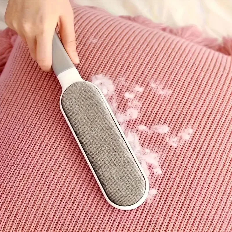 Una mano sostiene una herramienta para quitar pelo gris contra una tela texturizada rosa.
