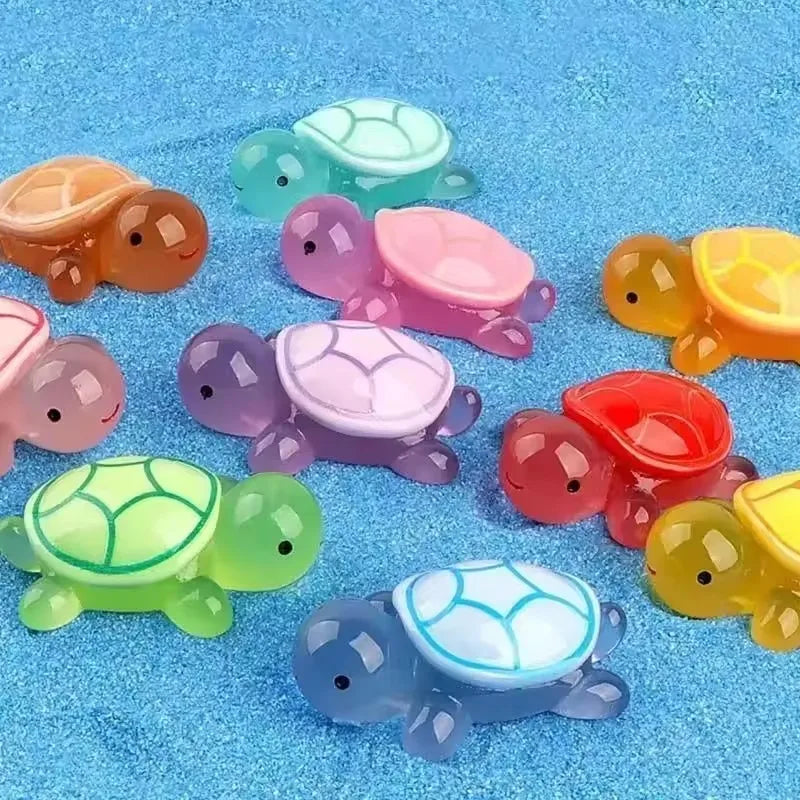 Eine Sammlung farbenfroher leuchtender Harz-Schildkrötenornamente in Grün, Pink, Gelb und Lila auf blauem Seegras