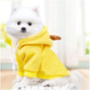 Un perro blanco vistiendo una sudadera amarilla con estampado de fruta, sentado sobre una superficie.