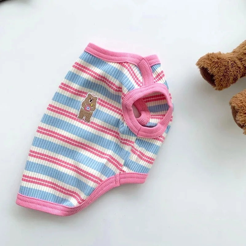 A pink and blue striped stretchy tank top for pets lying on a white surface.