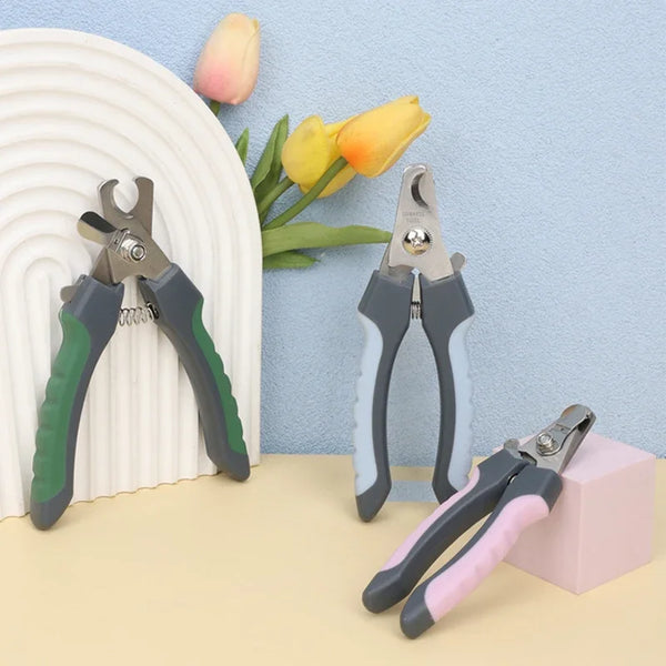 A collection of stainless steel pet nail clippers for dogs and cats in various shades of gray and green resting on a light su