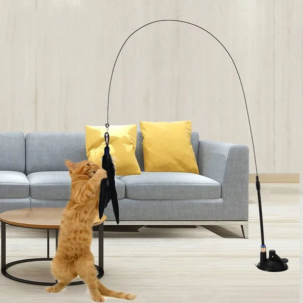 A golden cat is playing with a long, black suction cup wand toy in a modern living room setting.
