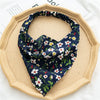A navy blue and white floral paisley triangle scarf is displayed on a light wood plate.