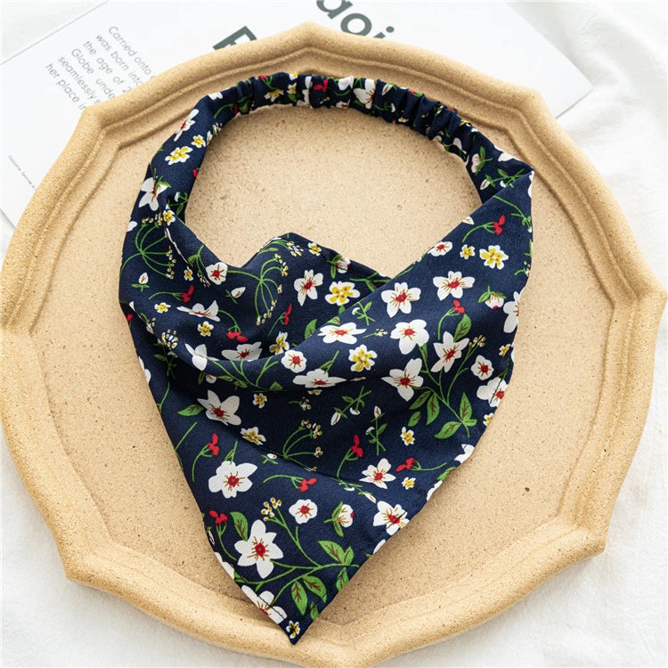 A navy blue and white floral paisley triangle scarf is displayed on a light wood plate.