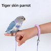 Une main tient un perroquet peau de tigre avec un harnais et une laisse violette.