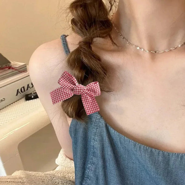 A close-up of a person wearing red plaid fabric bow hair clips in a ponytail, featuring a denim top.
